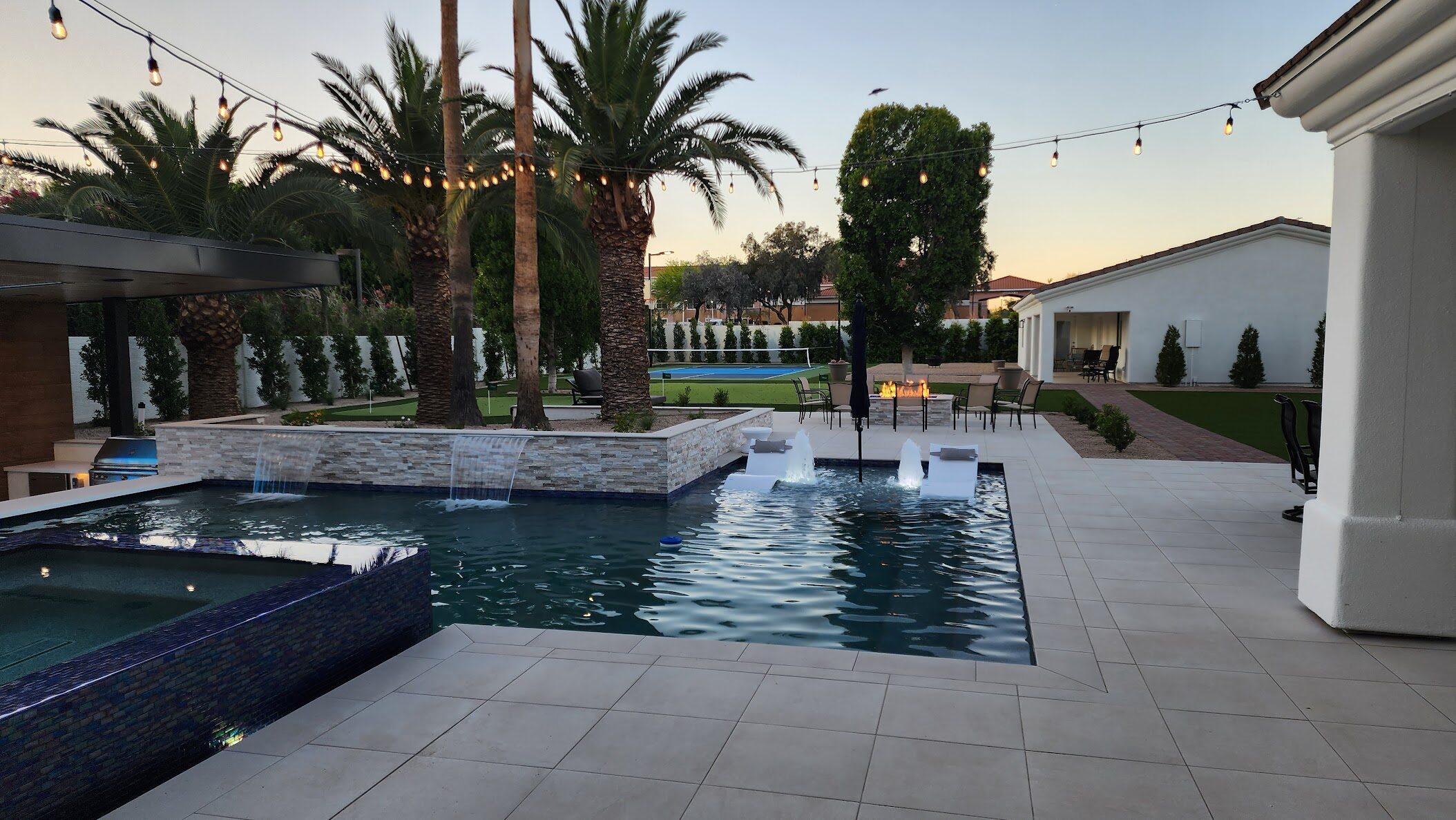 Paradise Valley resort estate pool with elevated spa, cascading waterfalls, stone features, outdoor living pavilion, and integrated landscape lighting at dusk